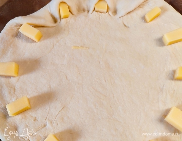 Тесто раскатать в круг диаметром 30 см. Сыр нарезать на 12 кусочков и разложить по кругу, защипать края.