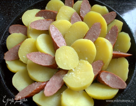 В той сковороде (22 см в диаметре), где жарился бекон, расположить ломтики картофели и между ними колбаску.