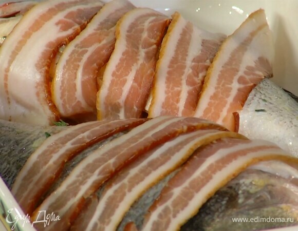 Оставшуюся половинку лимона порезать на кусочки и вложить в брюшки рыбы, сверху на дораду уложить полоски бекона.