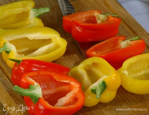 Сладкий перец, сохранив плодоножку, разрезать вдоль пополам, удалить семена с перегородками и выложить в жаропрочную керамическую форму плотно друг к другу.