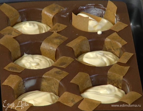 Формы для маффинов смазать сливочным маслом, вложить крест-накрест две полоски бумаги для выпечки, поместить на дно печенье, а сверху вылить сливочно-шоколадную массу, заполняя формы на 2/3 объема.