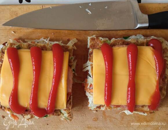 Теперь собираем сэндвичи. Хлеб посыпаем щепоткой сахара, кладем овощной квадрат, потом ветчину, пластинку сыра. Сверху поливаем кетчупом. Сверху кладем второй кусок хлеба и прижимаем несильно. Подержите минутку при нажатии, чтобы сэндвич потом не развалился.