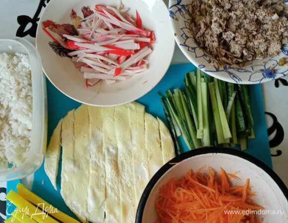 Пока варим/остужаем рис, подготавливаем остальные ингредиенты. Яйца взбиваем венчиком и жарим на растительном масле яичный блинчик на медленном огне под крышкой. Режем его на полоски. Морковь трем на терке для корейской моркови или режем тонкой соломкой. Заливаем морковь горячей подсоленной водой и даем постоять минут 10. Сливаем воду и обсушиваем морковь. Огурец режем на тонкие брусочки. Середину огурца не используем. Крабовые палочки разбираем на волокна или режем тонкими брусочками. Делаем начинку из тунца: содержимое банки (без жидкости) разминаем вилкой, добавляем мелко нарезанный маринованный огурец, заправляем майонезом. Майонеза должно быть немного. Начинка не должна быть жидкой. Дайкон уже замариновали брусочками.
