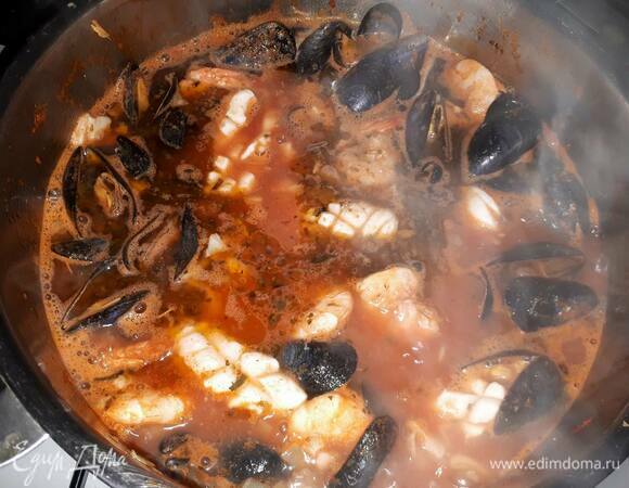 Затем добавьте оставшийся бульон, томатное пюре и обжаренные ранее морепродукты, размешайте и проварите 5 минут.