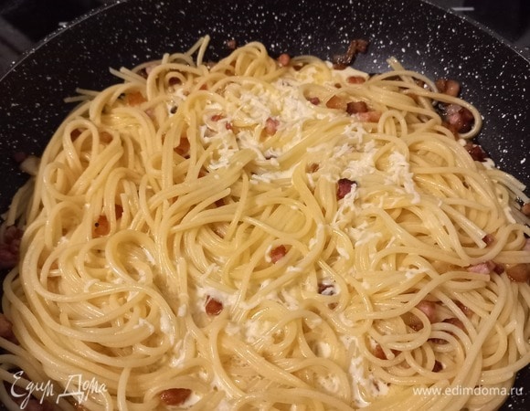 После готовности бекона отправляем в сковороду спагетти, перемешиваем. Через 1–2 минуты вливаем смесь желтка со сливками и сыром. На среднем огне слегка перемешиваем блюдо. Сверху поливаем 1 ст. л. оливкового масла. Соус в это время доходит до готовности от тепла сваренной пасты, поэтому готовим ингредиенты последовательно, а также не даем им остыть. Важно не передержать блюдо на данном этапе, иначе яично-сливочно-сырная масса свернется и блюдо будет сухим.