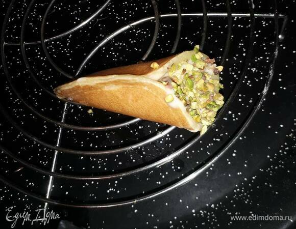 Взбейте крем на высокой скорости и наполните им блинчики. Обмакните каждый блинчик в рубленые фисташки и пропитайте сиропом.