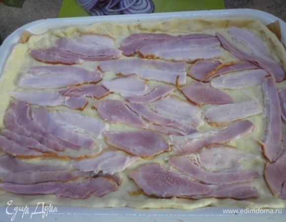 Духовку включить на 190°C. Тесто раскатать и выложить на противень (23 х 36), выстланный бумагой. Бекон нарезать тонкими ломтиками. Половину распределить по тесту.