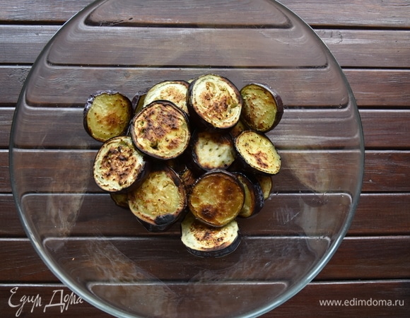 Сковороду разогреть на сильном огне. Добавить пару ст. ложек растительного масла, выложить порцию нарезанных баклажанов и обжарить с двух сторон до подрумянивания. Готовые кусочки выложить на салфетку для удаления излишка масла. Обжарить таким образом весь объем подготовленных овощей, по необходимости добавляя в сковороду растительное масло.