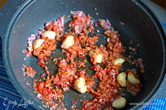 В выделившийся утиный жир выложить рубленый лук, дольки чеснока, соус чили ТМ «Махеевъ», посолить овощи и посыпать перцем, жарить 2–3 минуты.