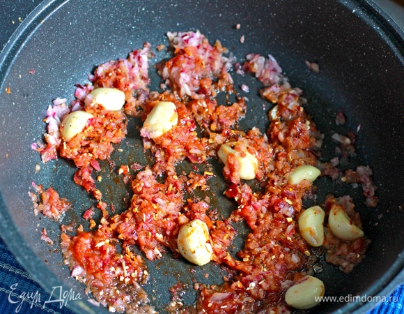 В выделившийся утиный жир выложить рубленый лук, дольки чеснока, соус чили ТМ «Махеевъ», посолить овощи и посыпать перцем, жарить 2–3 минуты.