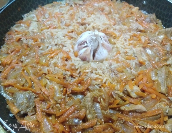 Когда вода выпарится до уровня риса, в середину плова положить головку чеснока. Углубить.
