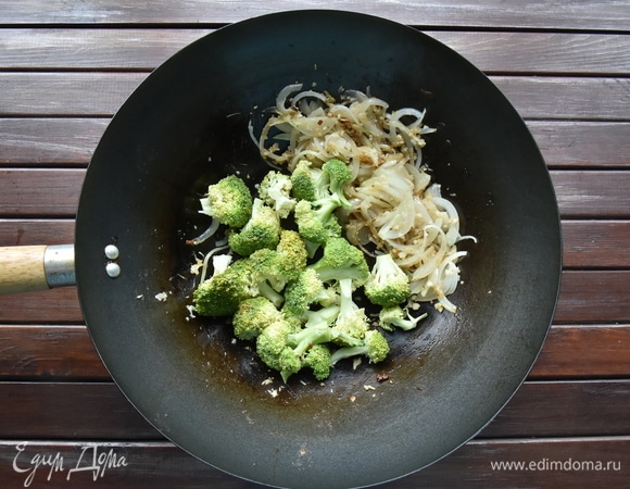 В том же воке на оставшемся масле обжарить имбирь, лук, чеснок в течение 30 секунд. Добавить соцветия брокколи. Огонь уменьшить до среднего и жарить овощи 1–2 минуты. Влить подготовленный соус. Увеличьте огонь и доведите соус до кипения.
