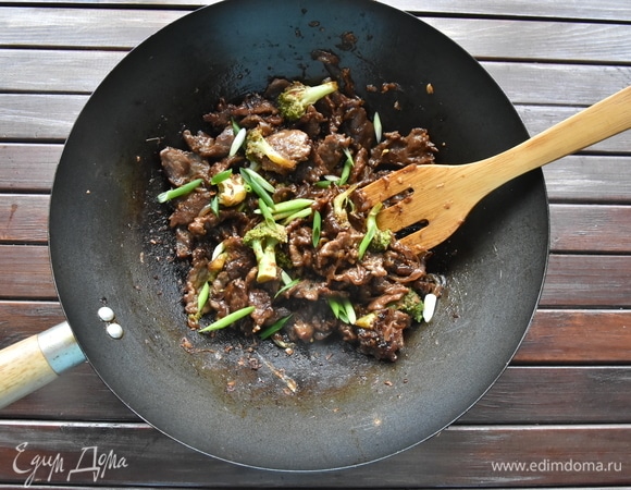 Когда соус начнет густеть, переложить к овощам обжаренную говядину и перемешать. Нагреть в течение 1 минуты и снять с огня. Добавить перья зеленого лука и соломку острого красного перца чили.