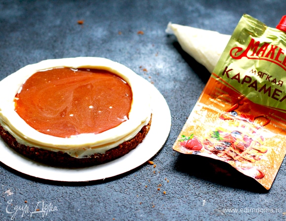 Для крема взбить холодный сыр с пудрой и сливками в плотную массу насадкой «весло», выложить в кондитерский мешок. Взвесить массу и разделить на 3 равные части. Я собираю торт на весах, чтобы соблюсти пропорции. Первый корж кладем на подложку, смазываем кремом и делаем бортик под начинку. В середину наливаем карамель ТМ «Махеевъ», закрываем вторым бисквитом.