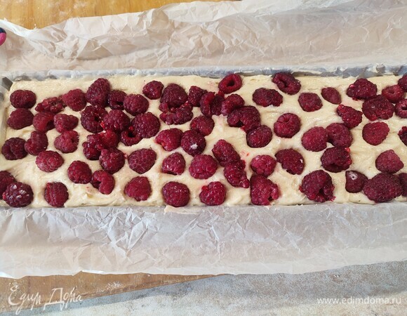 Выложить тесто в форму для выпечки, сверху выложить ягоды малины, слегка утопить в тесте. Выпекать 35 минут при температуре 180°C.