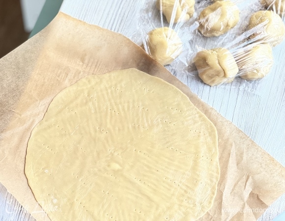 Охлажденное тесто разделить на 10 частей. Раскатывать кусочек и вырезать круг диаметром 22 см. Наколоть вилкой. Выпекать при 180°С вместе с обрезками пару минут до золотистости.