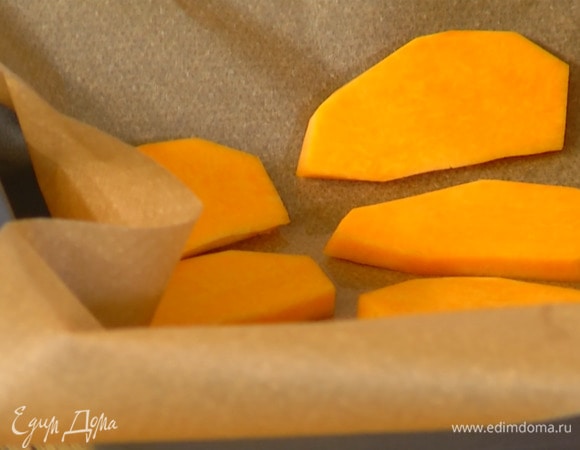 Тыкву почистить, нарезать ломтиками и выложить в один слой в глубокий противень, выстеленный бумагой для выпечки.