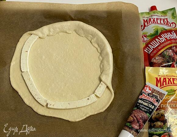 Одну часть раскатать в круг и по всему кругу, отступив от края 3 см, разложить нарезанные брусочки плавленого сливочного сыра. Края завернуть к центру.