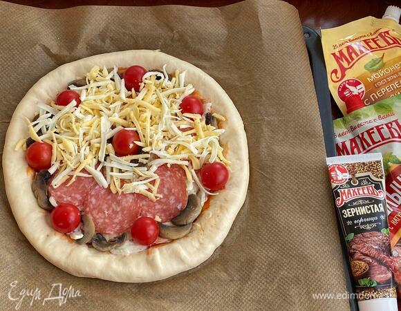Равномерно распределите нашинкованный лук, смешанный с майонезом и зернистой горчицей ТМ «Махеевъ». Разложите салями и обжаренные шампиньоны. По всей пицце распределите помидоры черри, посыпьте тертым сыром и поперчите. Выпекайте в разогретой до 190°C духовке 20–30 минут (ориентируйтесь на свою духовку).