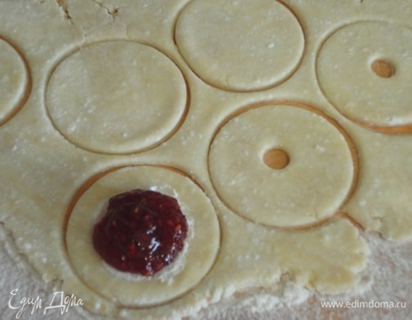 Включить духовку для разогрева на 160°C. Охлажденное тесто раскатать тонко и нарезать четное количество кружков. Половину смажьте по краю взбитым яйцом, выложите джем.
