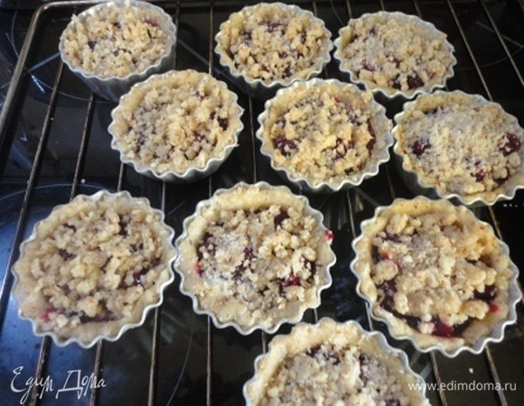 Тесто руками распределить по формочкам, формируя бортики. Заполнить их вишней и сверху посыпать протертой через терку миндальной крошкой. Выпекать 20–25 минут при 180–190°C.