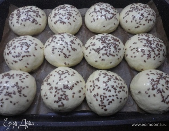 Когда булочки подойдут, взбейте яйцо с молоком и с помощью кондитерской кисточки смажьте поверхность булок, сразу же посыпая верх кунжутом или семенем льна.