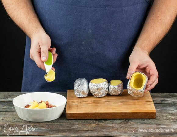 Когда картофель будет готов, аккуратно раскройте фольгу. Затем снимите с каждой картофелины верхушку и ложкой удалите часть мякоти, оставив по бокам толстые стенки.