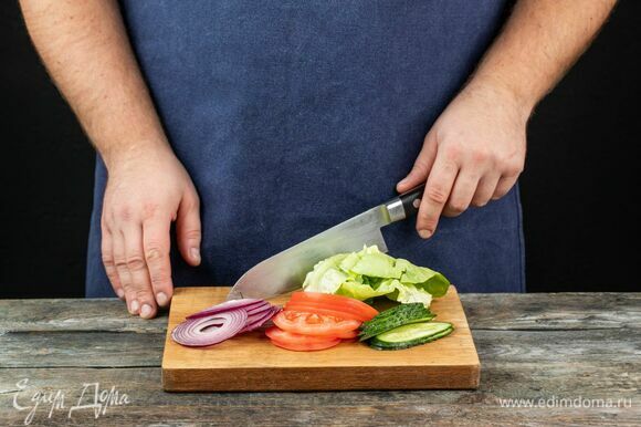 Подготовьте ингредиенты для бургера: тонко нарежьте свежие огурцы, помидоры и красный лук. Помойте и обсушите листья салата.