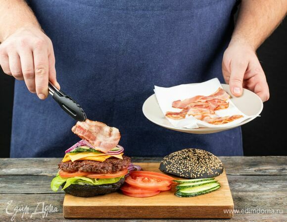 Соберите бургер: смажьте булочки белым соусом, выложите свежие огурцы, котлету с сыром, ломтики бекона, помидоры и свежий салат.