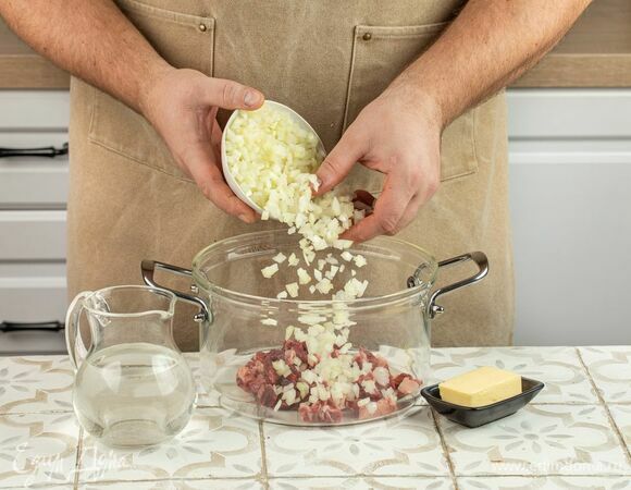 Нарежьте говядину поперек волокон на крупные кусочки. Переложите в кастрюлю. Измельчите лук. Чем мельче будут кубики, тем лучше. Отправьте к мясу.