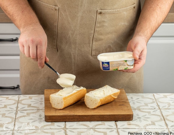 Разрежьте багет на порционные кусочки, а затем каждый вдоль. Утрамбуйте мякоть ложкой. Смажьте багет плавленым сыром Hochland «Сливочный».