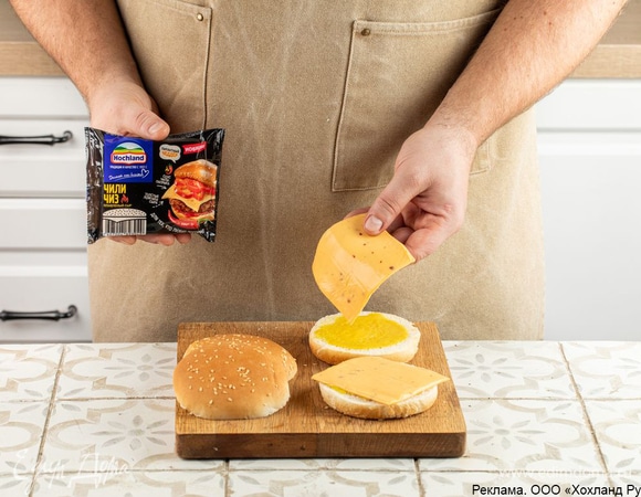 Разрежьте булочки пополам, смажьте каждую горчичным соусом. На все булочки выложите по толстому ломтику плавленого сыра Hochland «Чили Чиз». Толстые ломтики этого сыра сделают любой бургер или сэндвич пикантным, «сырным» и очень сочным! Отправьте заготовки в духовку, разогретую до 180°C. Подождите, пока сыр расплавится. Достаньте булочки и немного остудите.