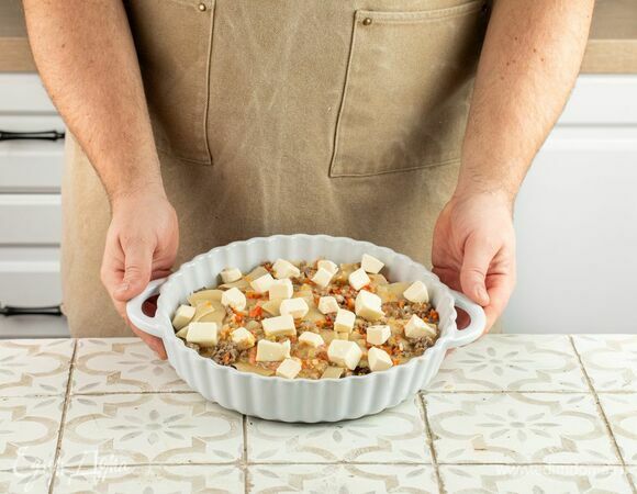 Посыпьте запеканку кубиками нарезанного сыра. Если начинка получилась сухой, влейте еще немного бульона. Отправьте в разогретую до 180°C духовку до расплавления сыра.