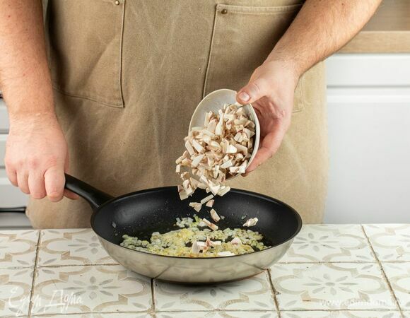 В это время мелко нарежьте лук и шампиньоны. Выложите в сковороду лук и слегка обжарьте, следом добавьте грибы, оставьте смесь на среднем огне под крышкой на 5 минут.