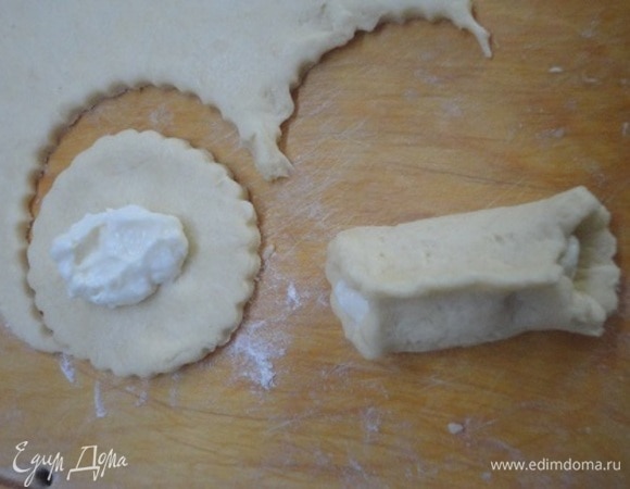 В миске взбиваем размягченное сливочное масло и сахарную пудру. Добавляем желток, кефир, щепотку соли. Хорошо перемешиваем все ингредиенты. Добавляем просеянную муку и разрыхлитель, замешиваем тесто. Оно получается мягким, но не добавляйте больше муки, только на стол, где будете раскатывать. Тесто нужно использовать сразу, не нужно давать ему отдыхать. Тесто раскатываем в пласт, вырезаем круги диаметром 8 см. В центр каждого круга выкладываем по 1 ч. л. начинки и формируем печенье. Защипываем очень хорошо.