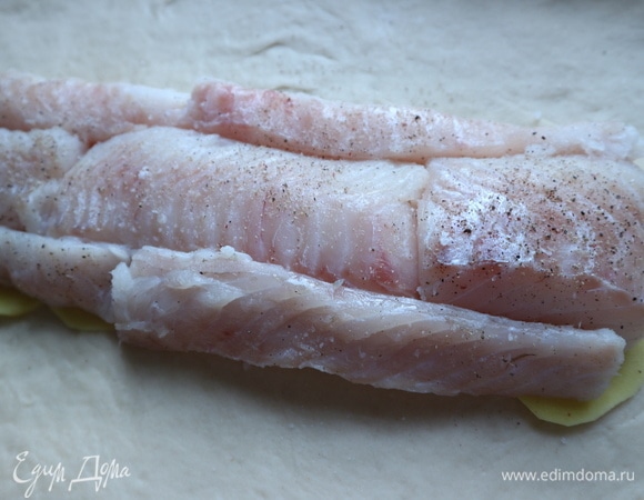 Если рыба влажная, предварительно промокнуть ее бумажным полотенцем, посолить, поперчить. На картофель поместить куски филе трески.