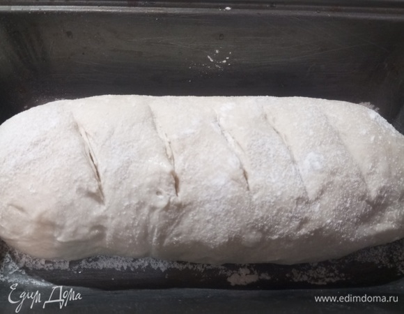 Форму посыпать мукой. Переложить заготовку, накрыть и оставить на 20–30 минут. Перед выпечкой смазать верх водой, сделать несколько неглубоких надрезов, слегка посыпать мукой.