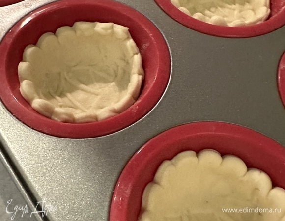 Раскатываем тесто, вырезаем круг и выкладываем в форму для маффинов. Ко дну принимаем стаканом, накалываем вилкой, смазываем яйцом и отправляем в духовку, разогретую до 180°C, на 17–20 минут. Либо берем готовые магазинные тарталетки.