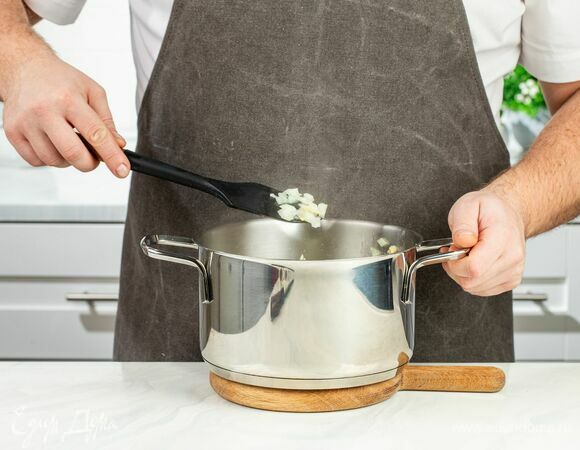 Нагрейте в кастрюле с толстым дном растительное масло и обжарьте в нем лук с чесноком до золотистого цвета.