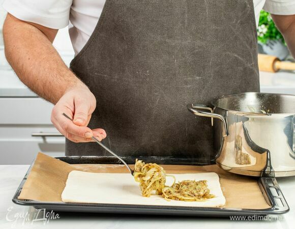 Тонко раскатайте пласт слоеного теста, выложите на него луковую начинку и заверните края. Добавьте оливки и отправьте пирог в духовку, разогретую до 180°С, на 20–25 минут.