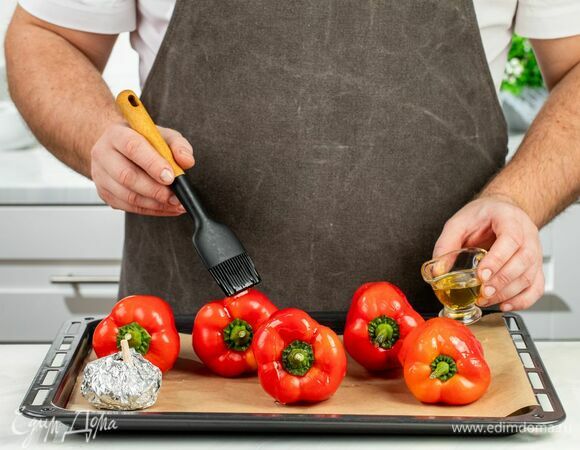 Перцы смажьте оливковым маслом, проткните вилкой и выложите на застеленный противень. Зубчики чеснока заверните в фольгу и положите рядом с перцами. Запекайте в духовке при 200°С в течение 25 минут.