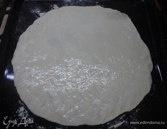 Подошедшее тесто тонко раскатайте на посыпанном кукурузной мукой столе в круг по размеру противня. У меня стандартный 40 х 40 см. Противень слегка припорошите кукурузной мукой и выложите на него раскатанное тесто. Смажьте его оставшимся оливковым маслом, оставляя чистым край теста.