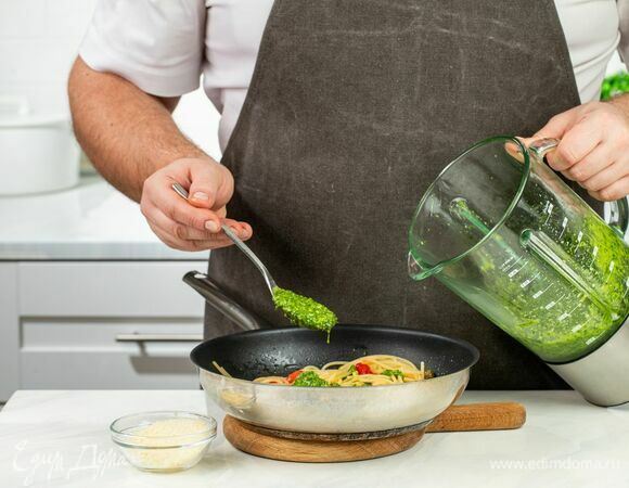 Добавьте соус песто, сохраненную воду, перемешайте и посыпьте тертым сыром.