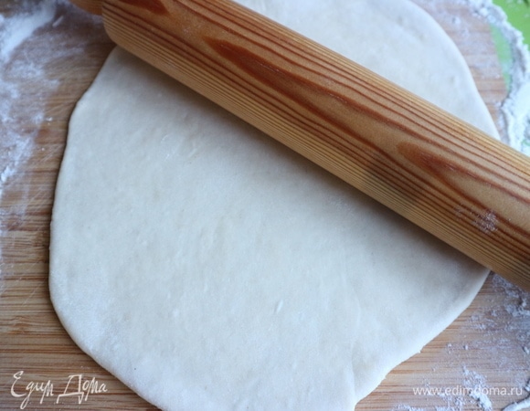 Раскатать скалкой тесто в тонкий пласт на рабочей поверхности, слегка посыпанной мукой.