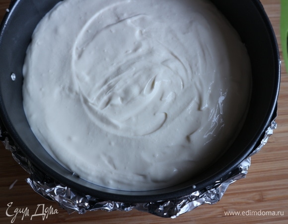 Достать форму из холодильника. Дать ей немного согреться. На всякий случай я обмотала разъемную форму фольгой. Духовку, в которую поставлена форма с водой (в самой нижней части духовки), разогреть до 140–150°C. Чизкейк будем делать в нижней третьей части духовки. Поместить в форму сырную массу, стараясь расположить ее равномерно по всей плоскости. Конвекцию не включать. Поставить форму в духовой шкаф на 1 час 20 минут. Вам может понадобиться чуть меньше или больше времени.