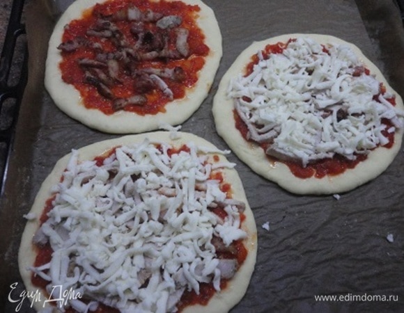 Тонко смазать поверхность каждой пиццы томатным соусом, оставляя чистым край теста. Сверху равномерно разложить бекон и накрыть все сыром моцарелла.