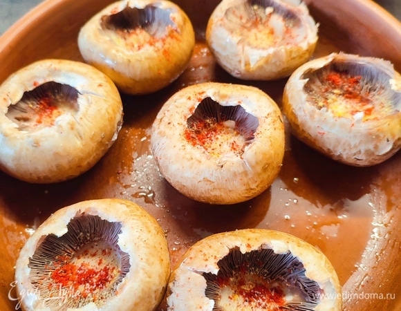 Шампиньоны почистить, убрать ножки. Сами шляпки посолить, можно посыпать любимыми специями. Выложить в форму для запекания, которая смазана подсолнечным маслом. Шляпки сбрызнуть подсолнечным маслом и поставить запекаться на 10 минут при 250°C.