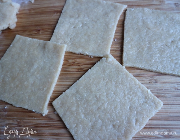 Достать тесто из холодильника, раскатать на рабочей поверхности, слегка посыпанной мукой, в пласт толщиной примерно 2 мм. Вырезать квадраты со стороной 10 см.