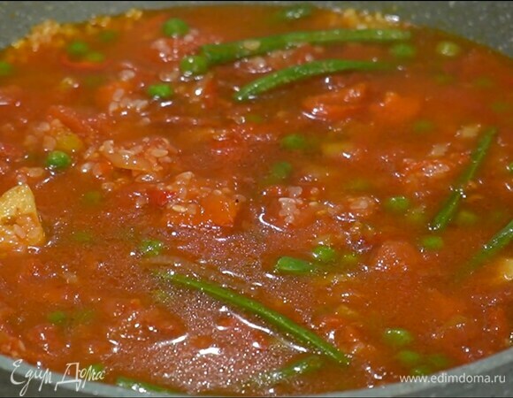 Фасоль, зеленый горошек и перец чили добавить в сковороду и перемешать, всыпать рис и еще раз перемешать, затем выложить помидоры в собственном соку, влить бульон и на медленном огне готовить 12–15 минут под крышкой.