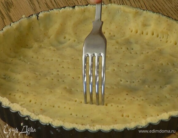 Форму для тарта смазать сливочным маслом и равномерно распределить тесто, сформировав бортики, затем часто наколоть его вилкой, накрыть бумагой для выпечки и всыпать любые бобовые.